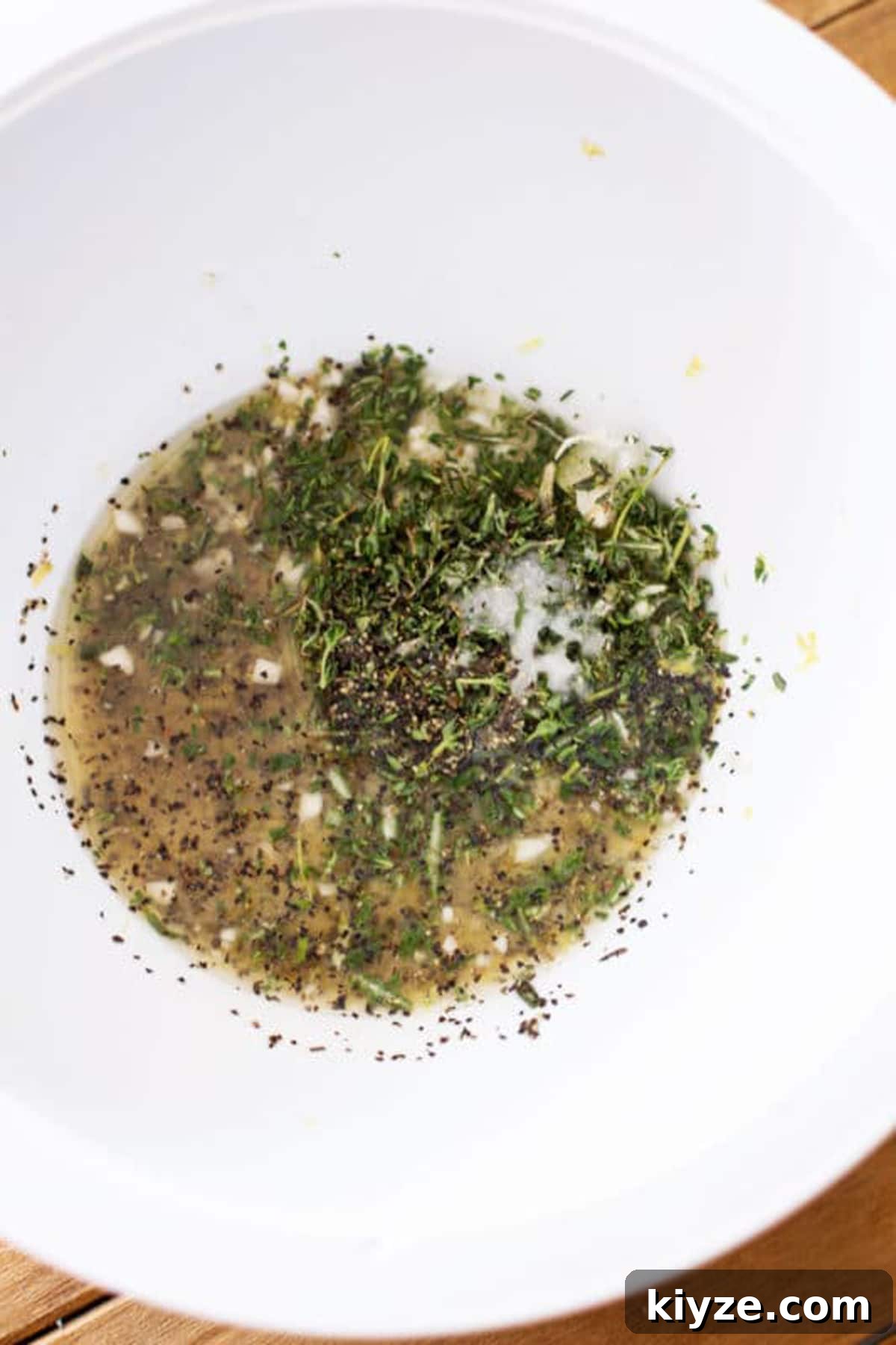 White bowl containing lemon juice, rosemary, thyme, salt and pepper for a Lemon Garlic Thyme Chicken recipe.