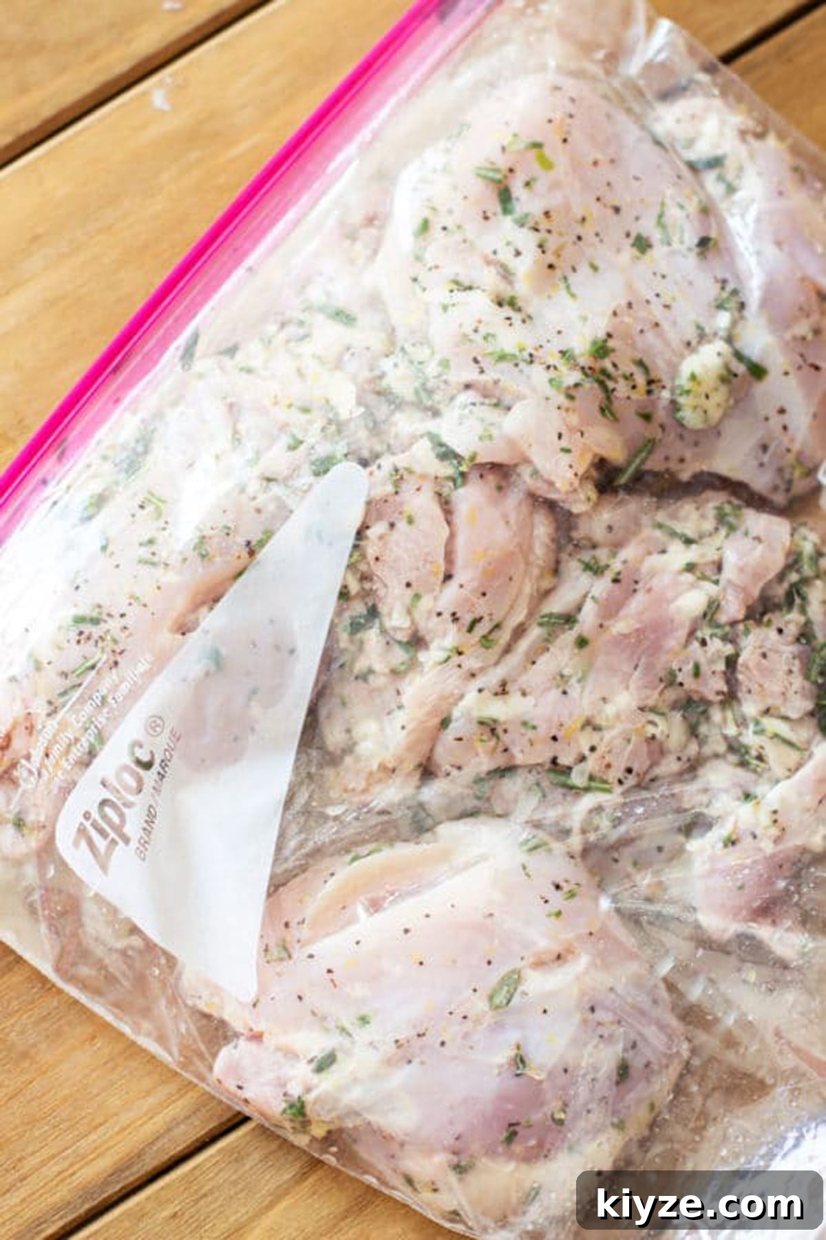 Large ziplock bag containing Lemon Thyme Garlic and Rosemary chicken thights and marinade on a brown table. 