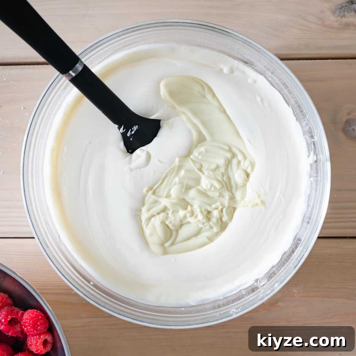 No-Bake Raspberry and White Chocolate Cheesecake Recipe 5 mixing bowl with whipped cream and mascarpone cheese and melted white chocolate.