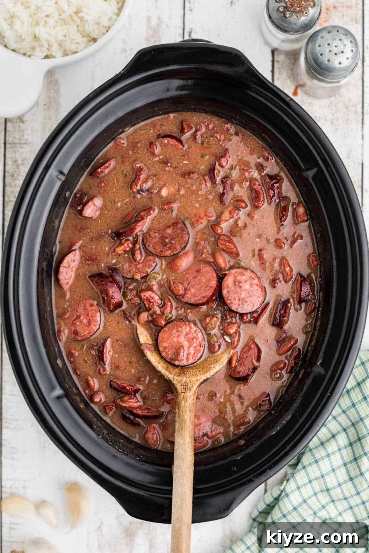 A spoon resting in a slow cooker with red beans and rice.