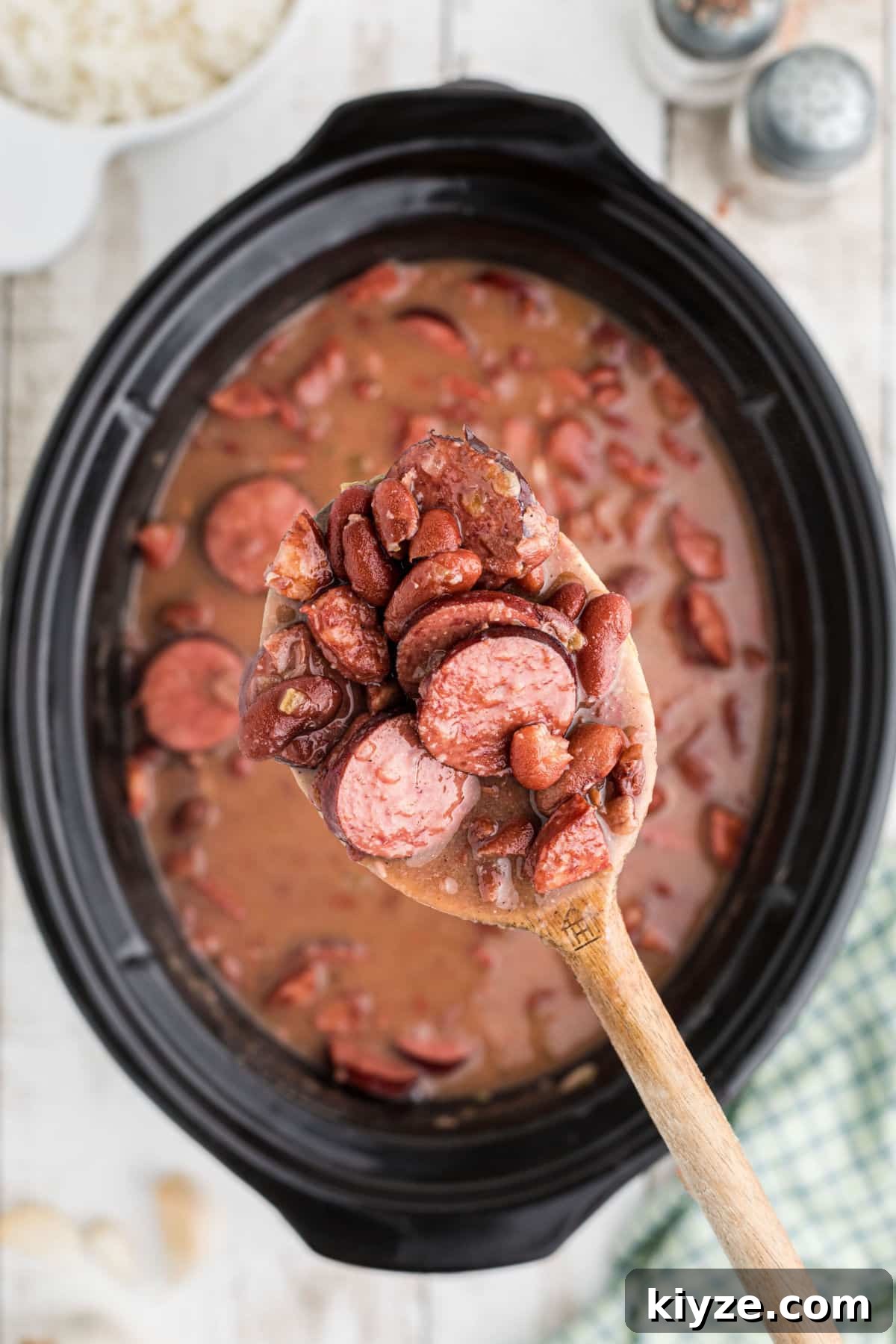 A spoon lifting some red beans out of a slow cooker.