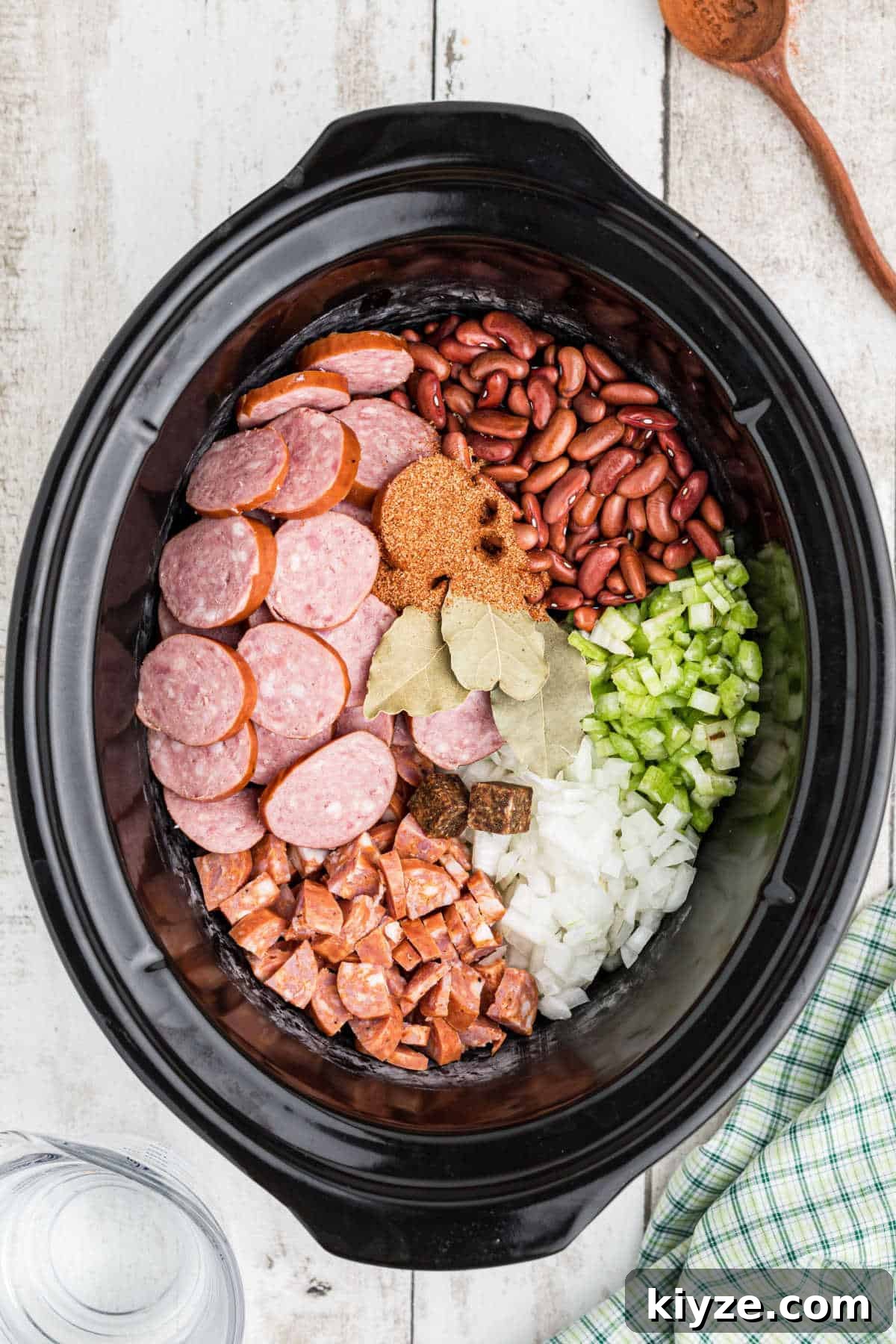 An overhead image of a crock pot filled with ingredients needed to make a Cajun red beans and rice recipe.