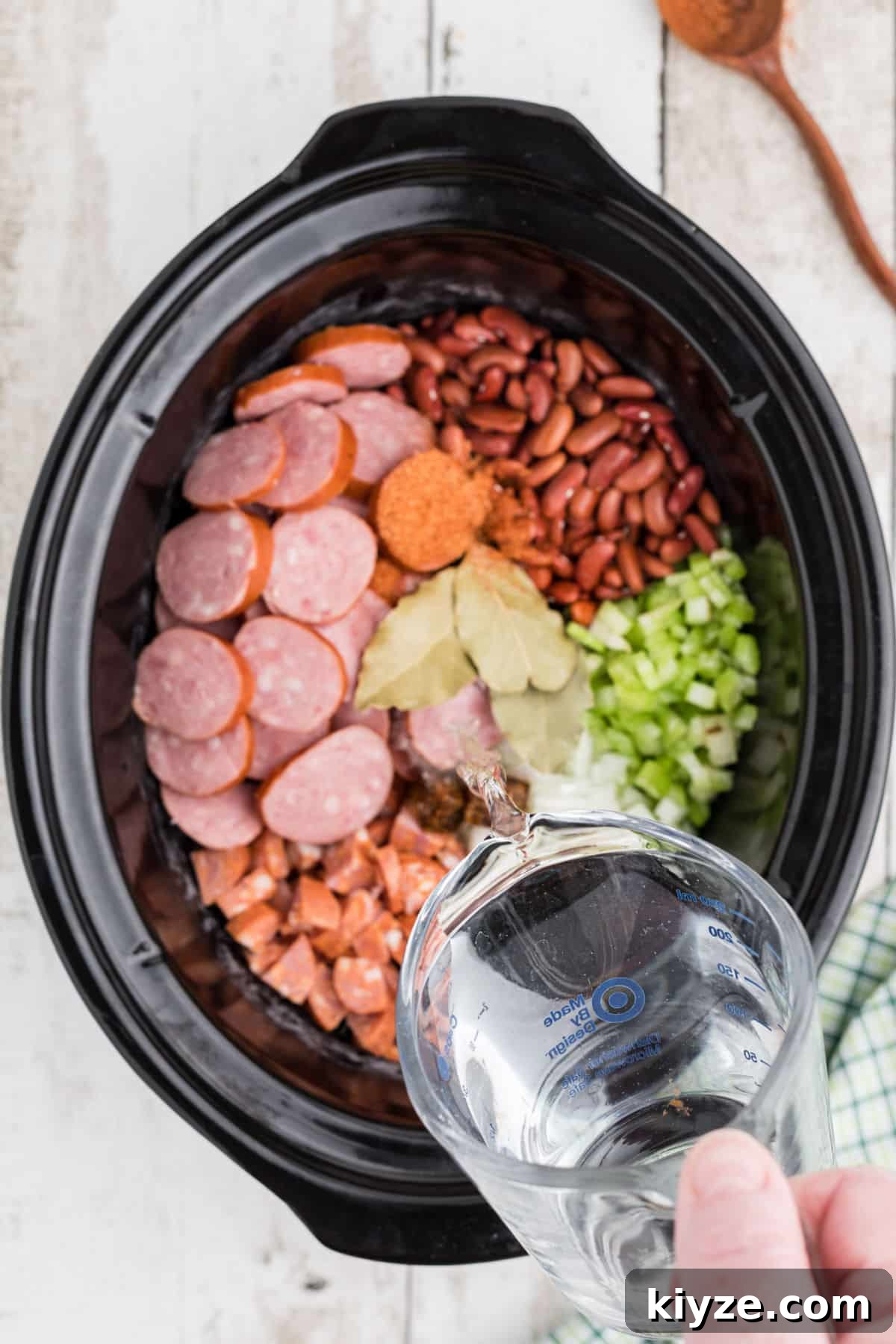 A slow cooker cajun red beans and rice recipe with water being poured in.