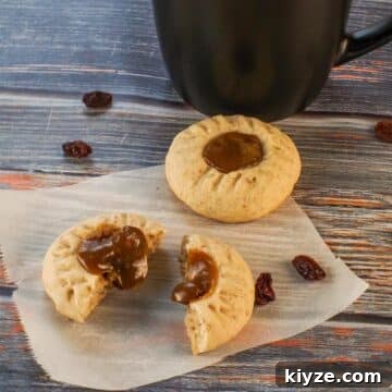 Butter tart cookies on parchment paper, with one split in half and filling oozing out. and black coffee mug in the background.