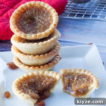 4 butter tarts stacked on a white plate, with a butter tart split in half in front of the stack