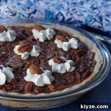 pecan pie in glass pie dish, on blue surface, with blue patterned oven mitts in the background