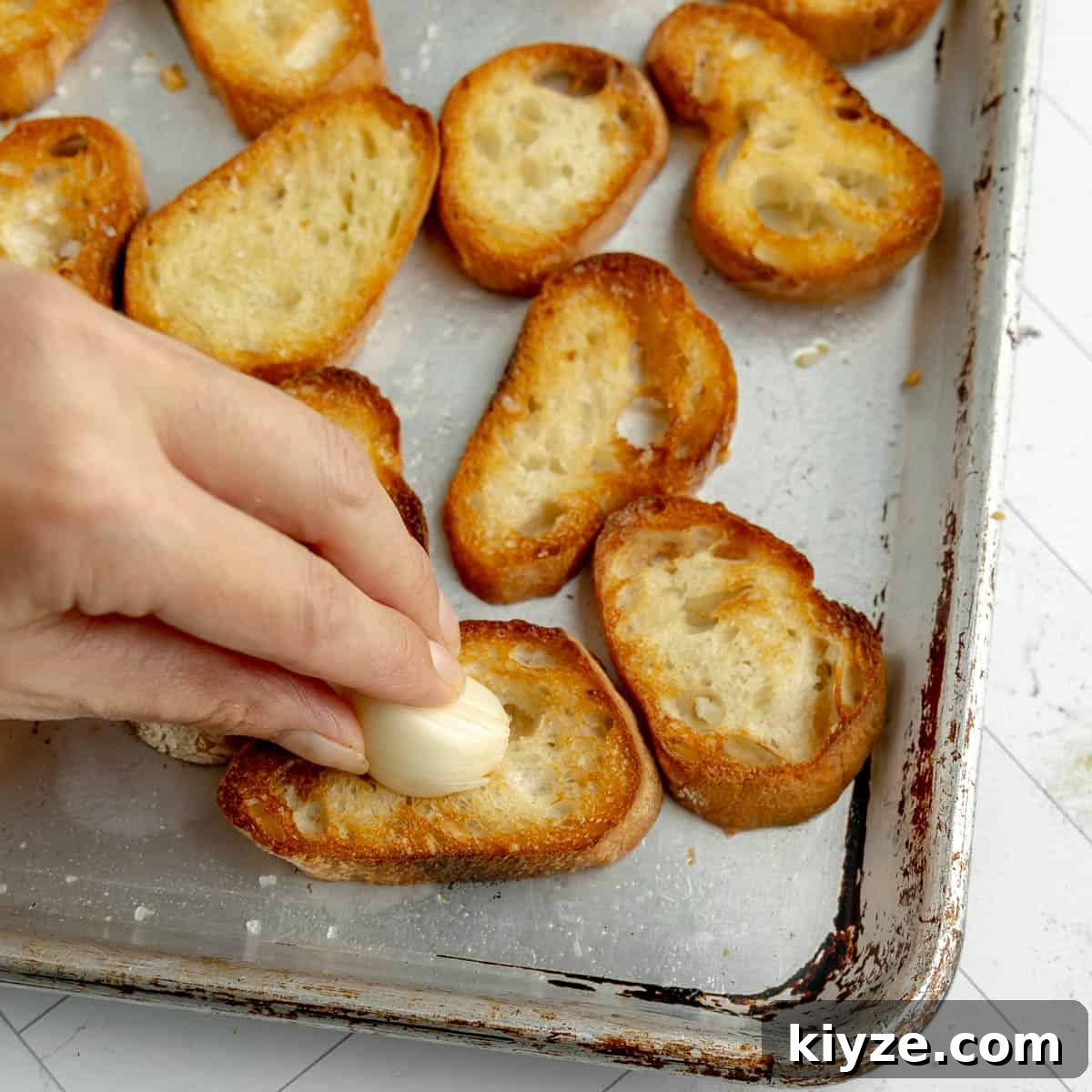 Crispy Garlic Crostini with Olive Oil and Herbs 8 A hand rubbing a garlic clove on toasts.