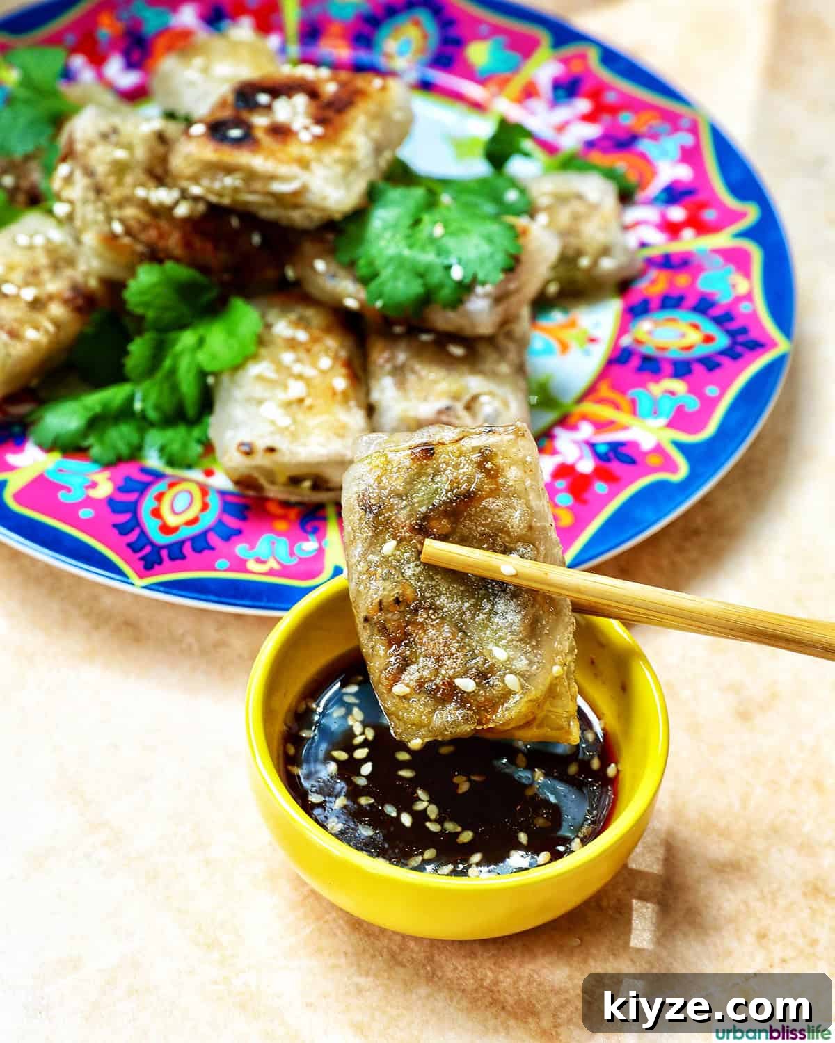 Crispy Rice Paper Dumplings with Savory Filling and Dipping Sauce 3 chopsticks holding a rice paper dumpling over a bowl of dipping sauce.