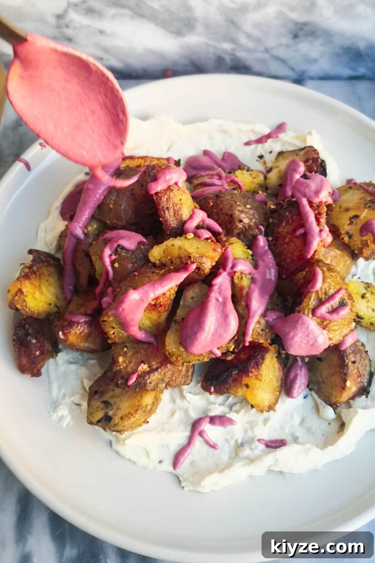 Crispy Dukkah Potatoes with Aioli & Pink Tahini Drizzle 12 A spoon drizzling pink tahini sauce over crispy dukkah potatoes on a plate with aioli.