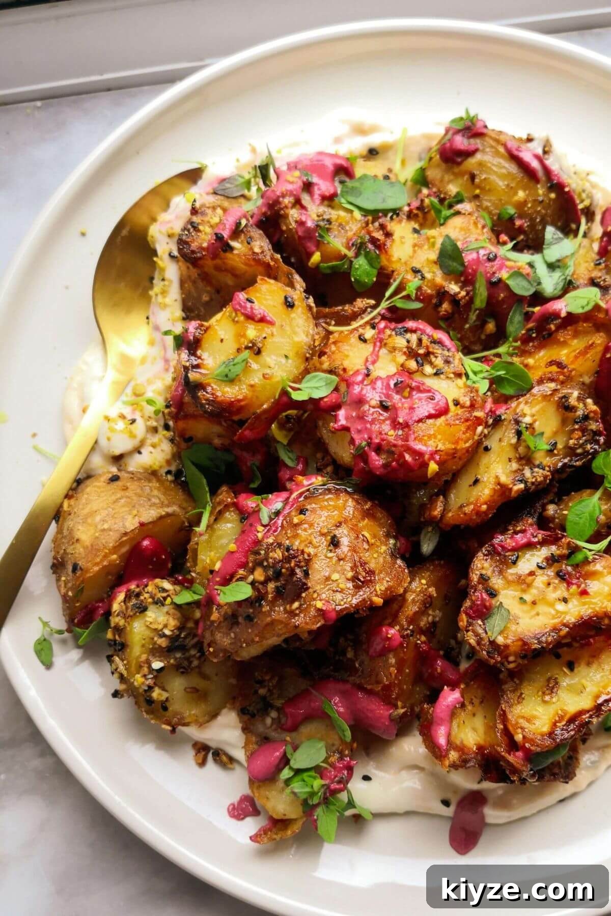 Crispy Dukkah Potatoes with Aioli & Pink Tahini Drizzle 13 Crispy dukkah potatoes on a white plate with a gold spoon, with thyme and pink tahini on top.
