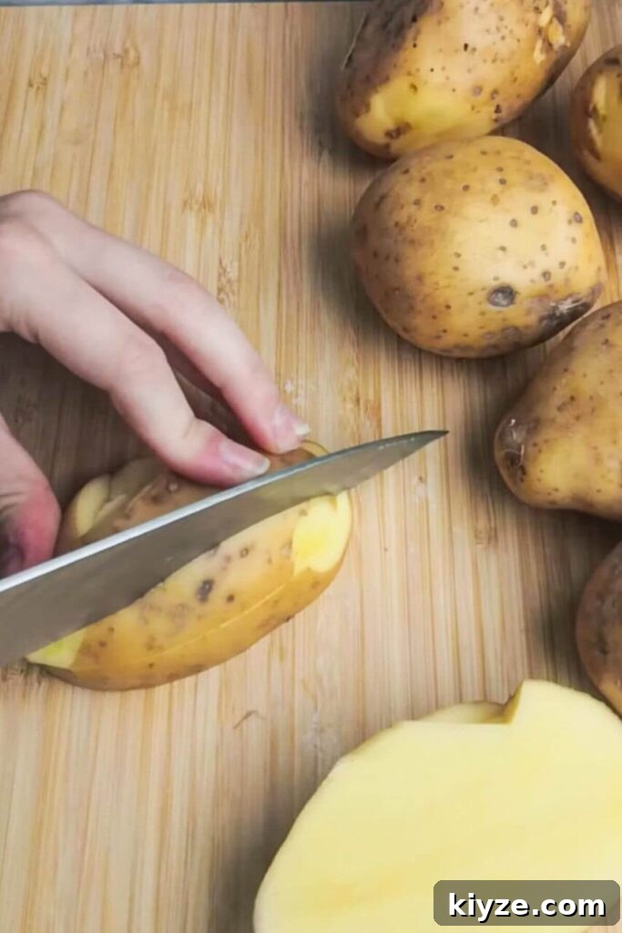 Crispy Dukkah Potatoes with Aioli & Pink Tahini Drizzle 3 A large knife slicing potato on a wooden board.