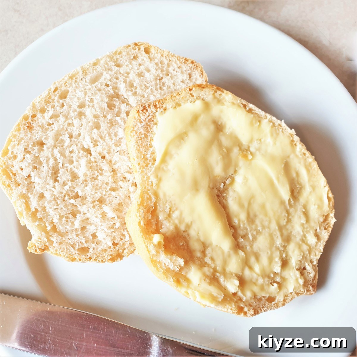 A breadroll split open and spread with butter on a white plate. A breadroll split open and spread with butter on a white plate.