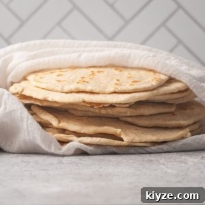 stack of homemade fluffy flour tortillas wrapped in a kitchen towel