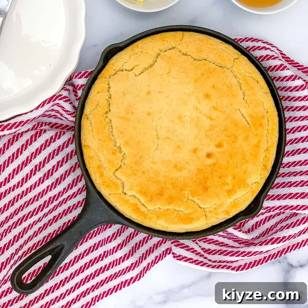 Jiffy Cornbread with Creamed Corn Casserole Recipe 5 a cast iron skillet with cornbread with self rising flour and a striped red kitchen towel at the back.
