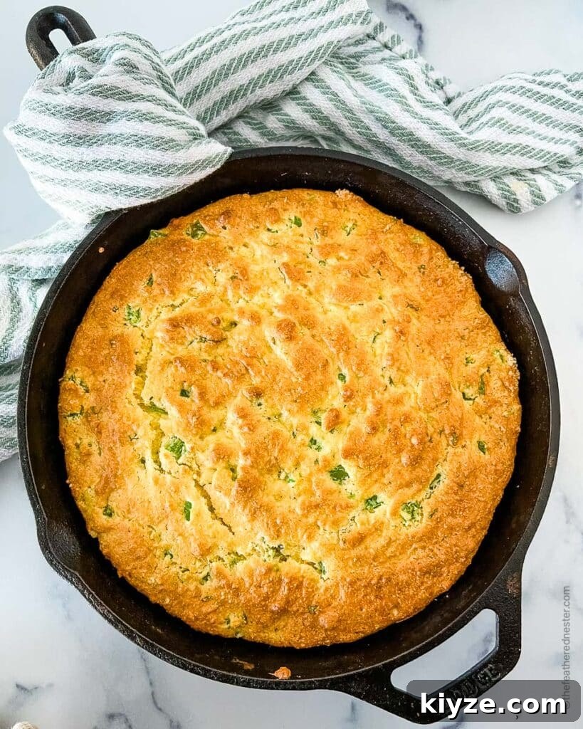 Jiffy Cornbread with Creamed Corn Casserole Recipe 10 baked Jiffy jalapeno cheddar cornbread in a skillet with a striped cloth in the background.