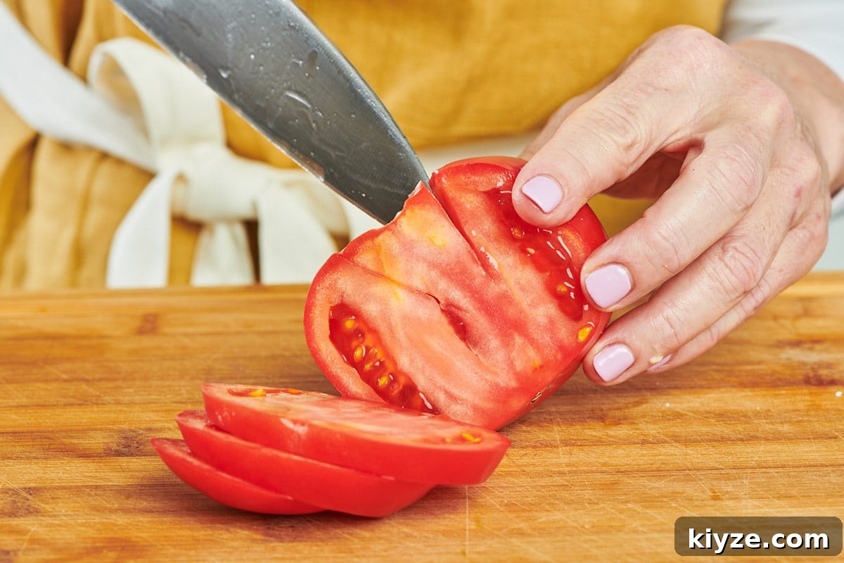 How to Slice and Dice Tomatoes Like a Pro 4 Katie Workman cutting stem out of large ripe tomato with knife on cutting board.