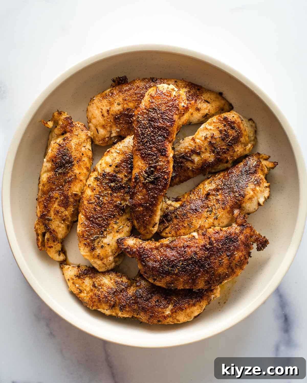 Cajun Blackened Chicken Tenders with Zesty Dipping Sauce 2 Blackened chicken tenders in a white bowl on a table.