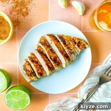 Sliced Tajín Grilled Chicken sits on a white plate surrounded by Tajín seasoning, a sliced lime, a white linen, and a small glass of beer.
