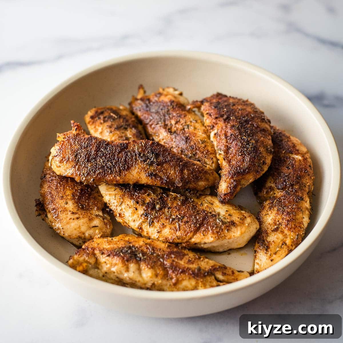 Cajun Blackened Chicken Tenders with Zesty Dipping Sauce 9 Blackened chicken tenders in a white bowl on a marble table.
