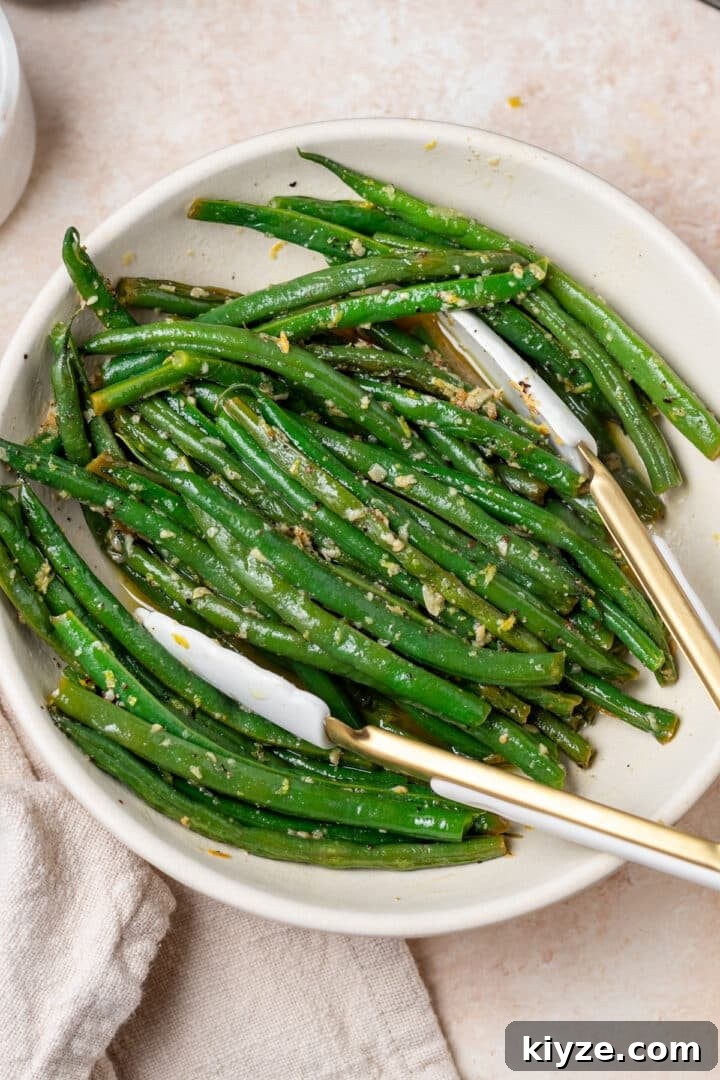 white serving bowl with lemon butter garlic green beans, white and gold tongs