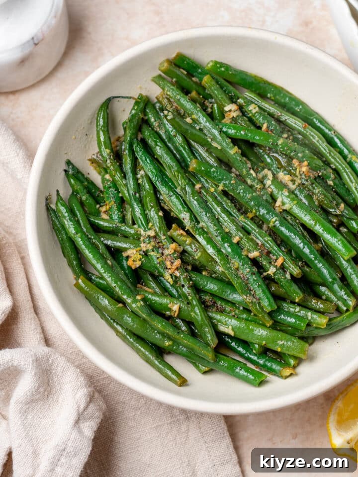white bowl with cooked green beans specked with lemon zest and minced garlic