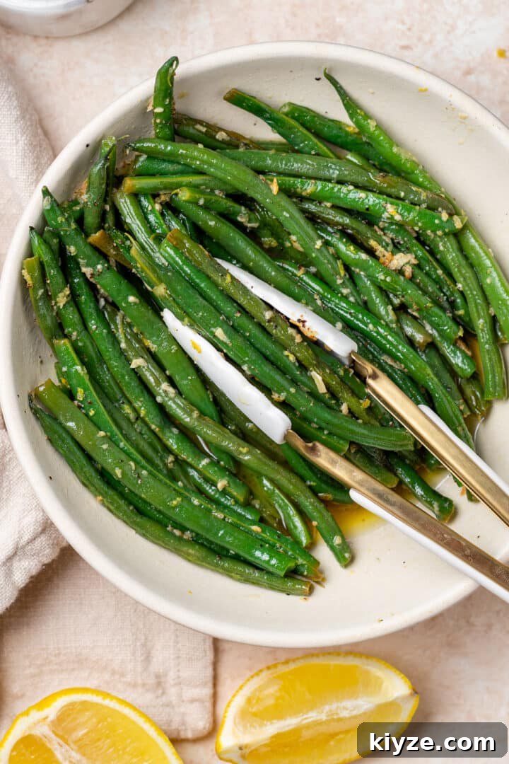 tongs grabbing a portion of haricot verts from a white serving bowl