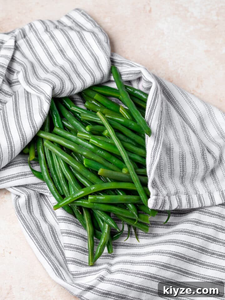 cooked green beans being patted dry with a gray striped kitchen towel