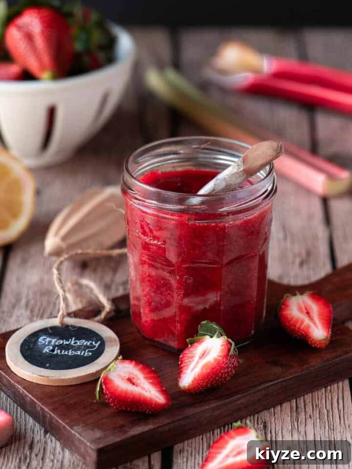 Small-Batch Strawberry Rhubarb Jam Recipe for Preserving Summer Flavor 2 Strawberry rhubarb jam in a clear jar on a wood surface with fruit around it.