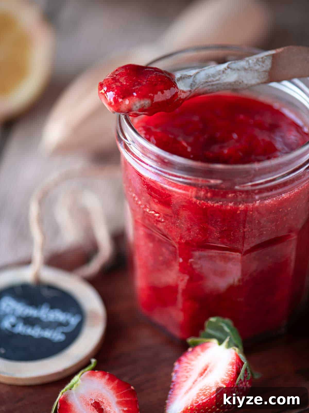Small-Batch Strawberry Rhubarb Jam Recipe for Preserving Summer Flavor 5 Close up of a spoon dipped into strawberry jam in a clear jar.