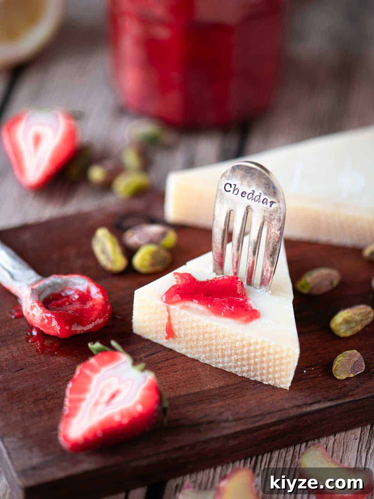 Small-Batch Strawberry Rhubarb Jam Recipe for Preserving Summer Flavor 6 Strawberry rhubarb jam on a wedge of cheese on a wooden board.