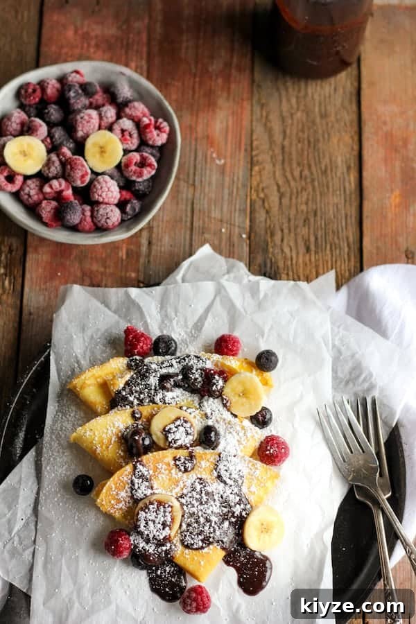 Gluten-Free Coconut Flour Crepes Recipe 2 Photo shows a plate of crepes covered in chocolate and powdered sugar next to a bowl of berries
