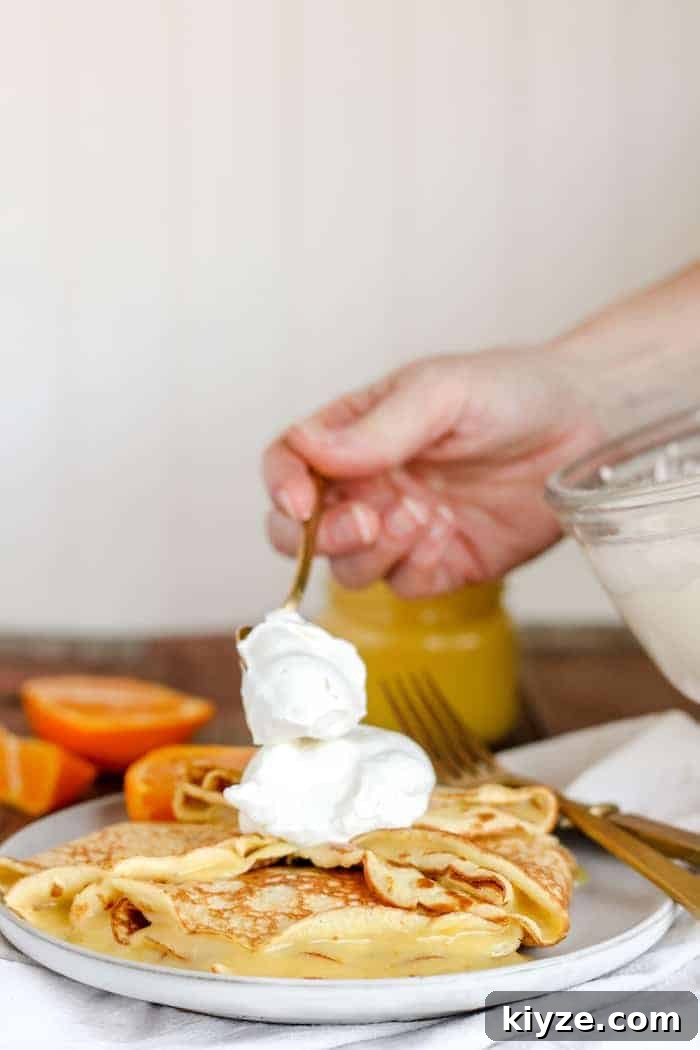 Gluten-Free Coconut Flour Crepes Recipe 5 Image shows a hand placing orange curd on crepes