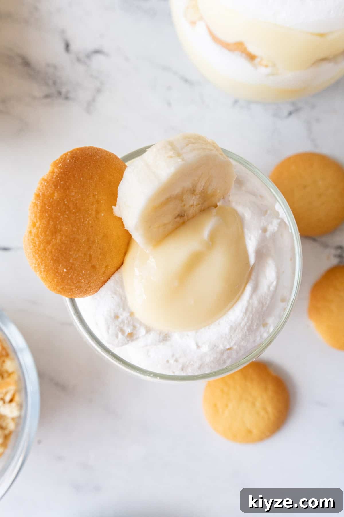 top of pudding cup filled with layers of pudding, whipped cream, cookies, and banana slices, with a banana slice and a cookie as a garnish.