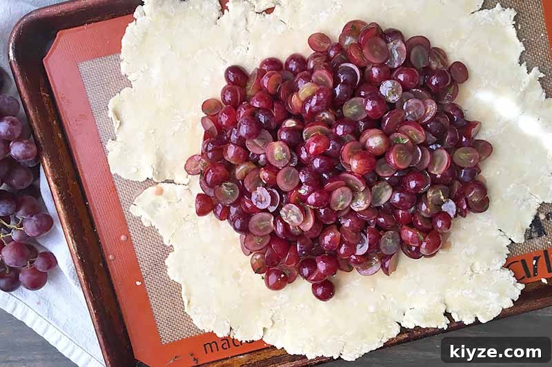 Grape Galette: Turn Fresh Grapes into a Rustic Dessert 12 Horizontal image of a pile of sliced grapes on rolled out pie dough.
