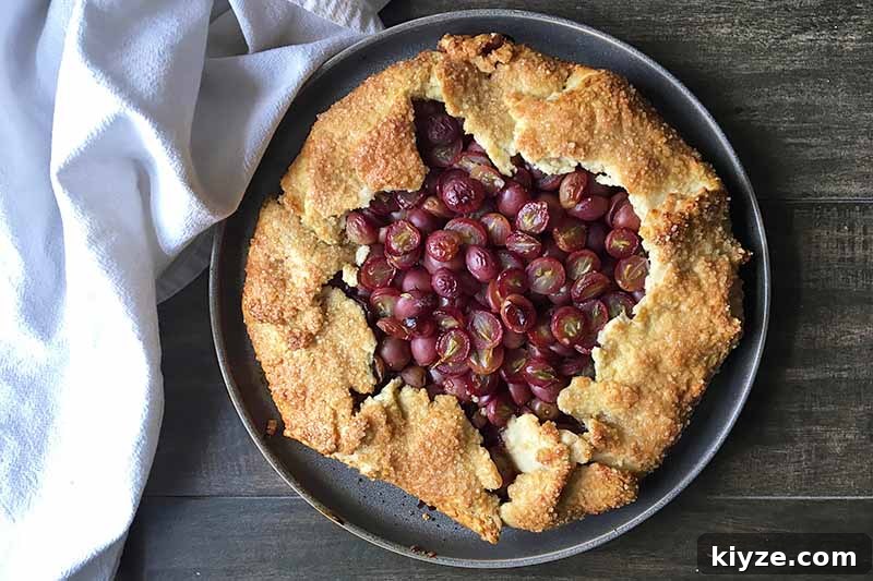 Grape Galette: Turn Fresh Grapes into a Rustic Dessert 15 Horizontal image of a whole baked galette with grapes on a gray plate next to a white towel.