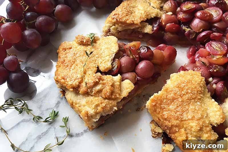 Grape Galette: Turn Fresh Grapes into a Rustic Dessert 16 Horizontal image of a whole galette with one slice out of it, next to fresh grapes and thyme leaves.