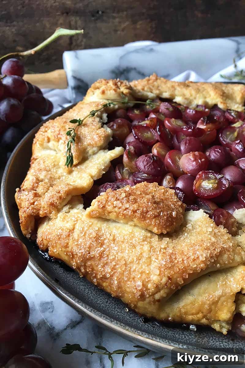 Grape Galette: Turn Fresh Grapes into a Rustic Dessert 3 Vertical image of the sugary crust of a grape galette on a gray plate, with a rolling pin in the background.