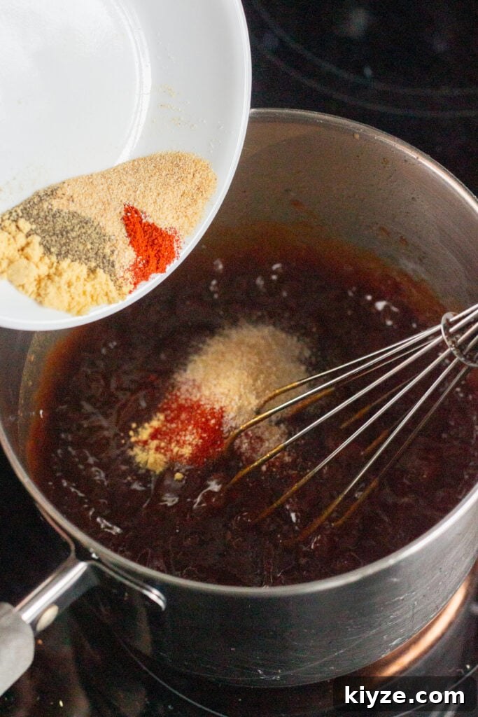 20-Minute Apricot Barbecue Sauce with Sweet and Tangy Flavor 5 Close up of a pot with ingredients for apricot bbq sauce in it, with spices being poured out of a white plate into the pan. The pan also has a whisk in it.