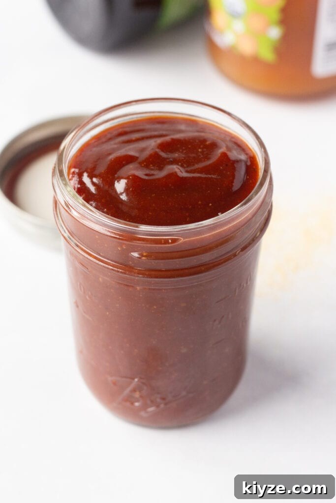 20-Minute Apricot Barbecue Sauce with Sweet and Tangy Flavor 6 Close up of a small mason jar with apricot barbecue sauce in it on a white surface. In the background are jars with jam and molasses in them.