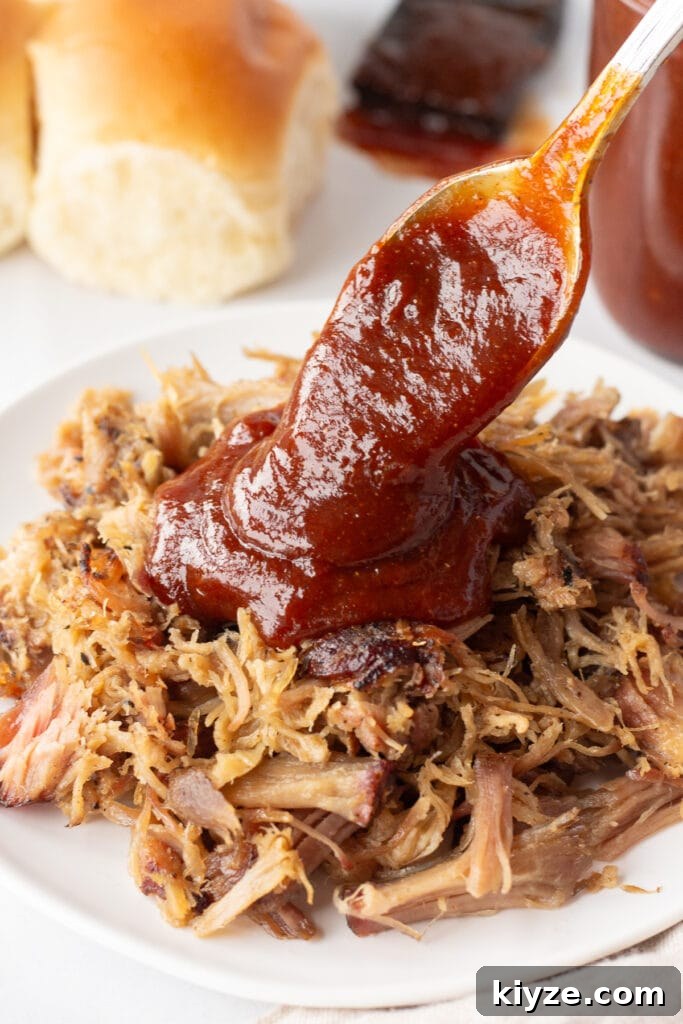 20-Minute Apricot Barbecue Sauce with Sweet and Tangy Flavor 7 Close up of apricot barbeque sauce being poured over a white dish with pulled pork on it with a spoon.