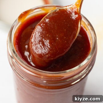 20-Minute Apricot Barbecue Sauce with Sweet and Tangy Flavor 9 Close up of apricot barbecue sauce in a small mason jar with a spoon dipping in it.