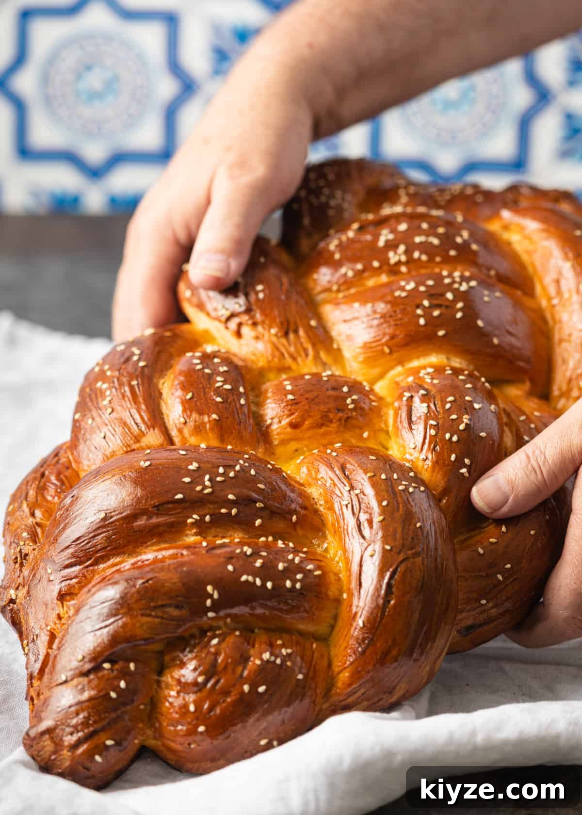 Classic Fluffy Challah Recipe for Braiding and Baking 3 closeup view: hands holding challah lifted above tea towel