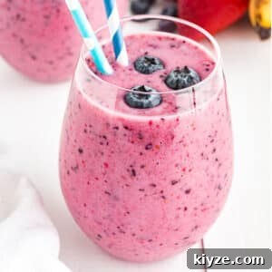 Glass of blueberry smoothie with blueberries and a straw.