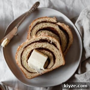 Cinnamon Swirl Bread with Crumbly Streusel Topping 11 A closeup of two slices of cinnamon swirl bread topped with a pat of butter on a white plate with a butter knife placed on a white table cloth next to a beige linen.