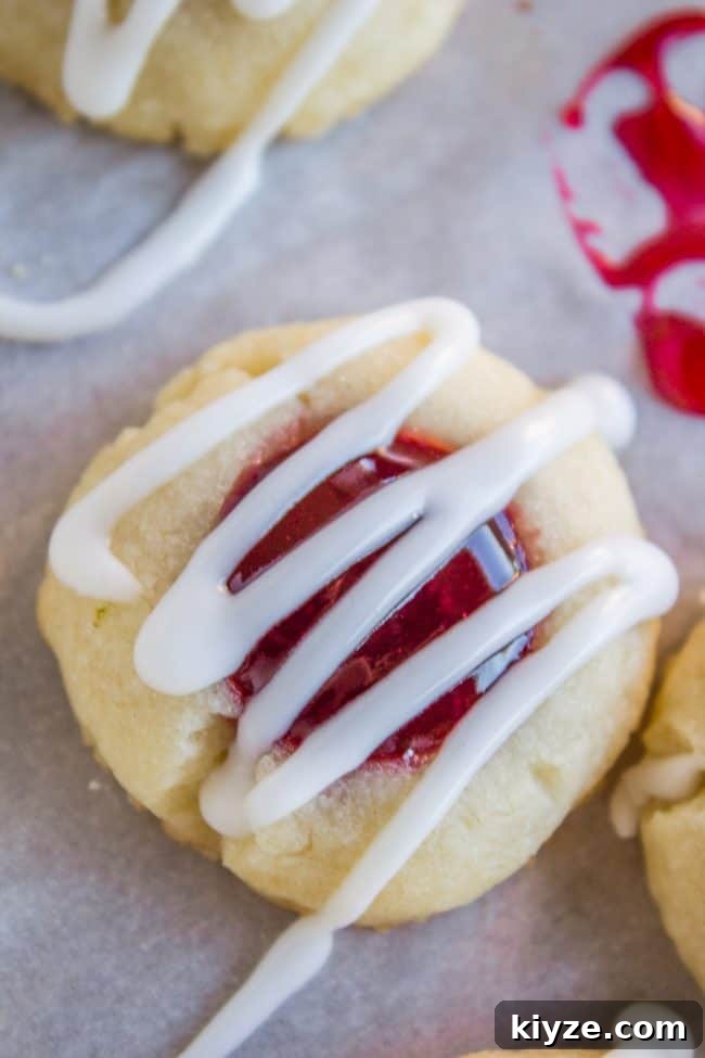 Almond Raspberry Thumbprint Cookies: Chewy Jam-Filled Recipe 2 Raspberry Thumbprint Cookie with glaze on parchment paper.