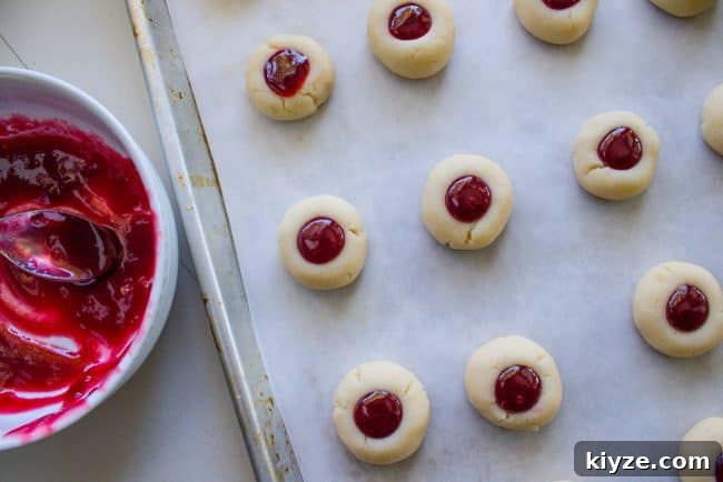 Almond Raspberry Thumbprint Cookies: Chewy Jam-Filled Recipe 12 cookies laid out on baking sheet filled with raspberry jam.
