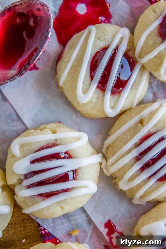 Almond Raspberry Thumbprint Cookies: Chewy Jam-Filled Recipe 3 raspberry jam thumbprint cookies with glaze drizzled on top.
