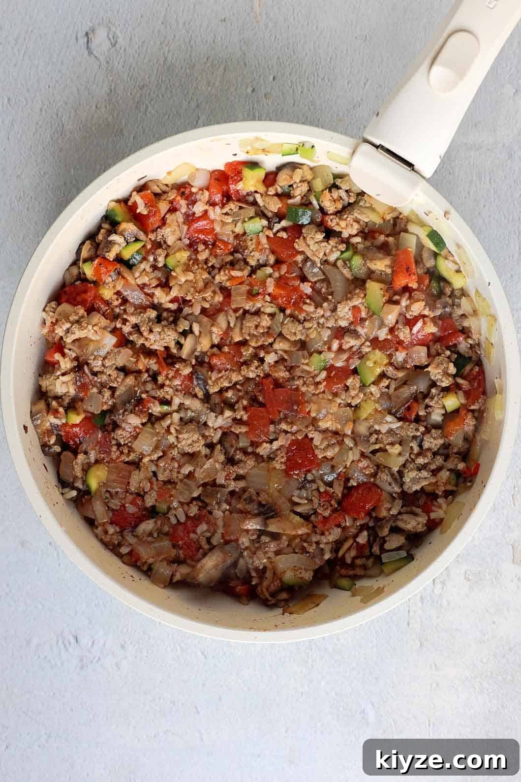 Ground Turkey and Rice Stuffed Bell Peppers Recipe 7 Turkey mixture in a skillet including ground turkey, diced onion, diced mushrooms, diced zucchini, fire roasted tomatoes, cooked rice, and seasoning.
