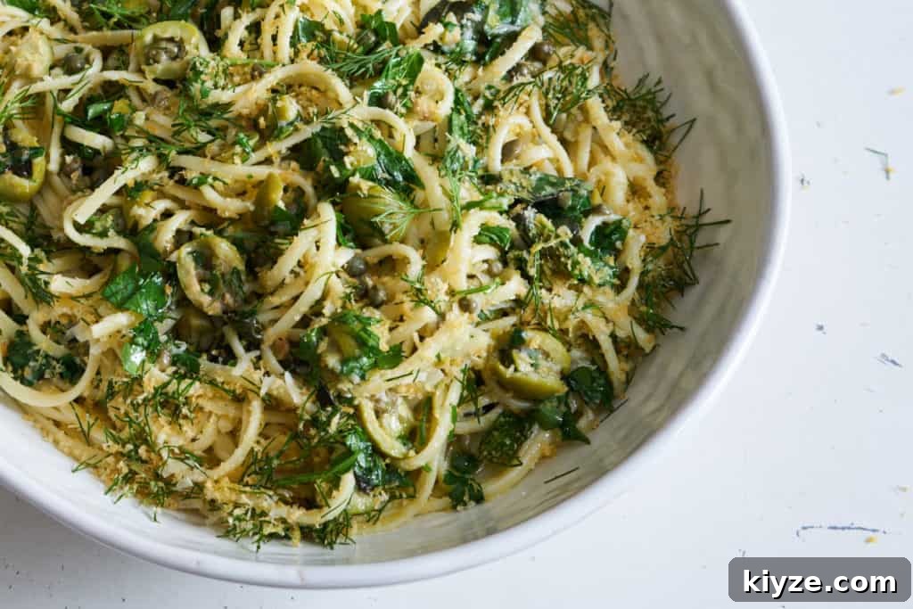Pasta with Green Olives, Capers & Fresh Herbs Recipe 2 Linguine pasta with green olives, herbs, and capers topped with bread crumbs in a white bowl sitting on a white surface.