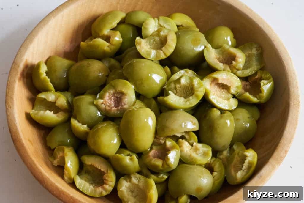 Pasta with Green Olives, Capers & Fresh Herbs Recipe 3 A wooden bowl full of Castelvetrano olives that have been torn in half.